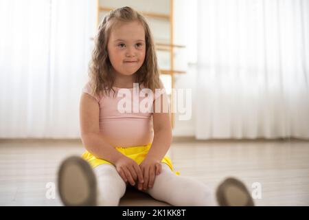 Little girl with down syndrome at ballet class in dance studio,sitting and resting. Concept of integration and education of disabled children. Stock Photo