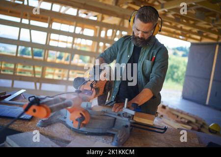 Construction worker working with eletric saw inside wooden construction of house, diy eco-friendly homes concept. Stock Photo