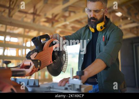 Construction worker working with eletric saw inside wooden construction of house, diy eco-friendly homes concept. Stock Photo