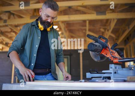 Construction worker working with eletric saw inside wooden construction of house, diy eco-friendly homes concept. Stock Photo