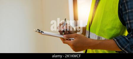 close up hands of inspector wear safety vest and checking list into clipboard, Architect Checking Insulation During House Construction Stock Photo