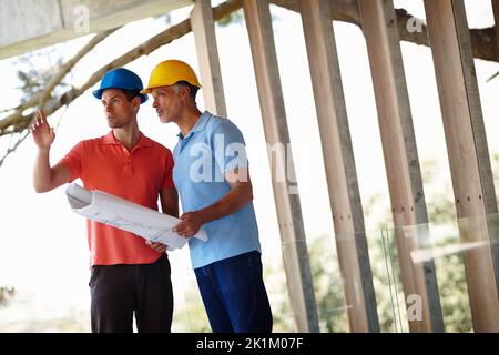 I have no idea what his showing me....Two architects standing on site reading from the blueprint. Stock Photo