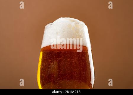 One glass amber golden beer overflowing against brown  background Stock Photo