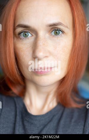 Young pretty woman with red hair, green eyes and freckles looks carefully at the camera. Close-up, selective focus. Stock Photo