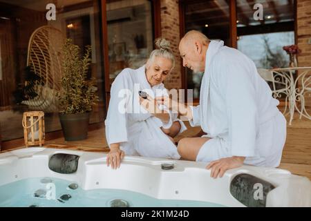 Senior couple prepare outdoor bath tub and chcecking smartphone. Stock Photo