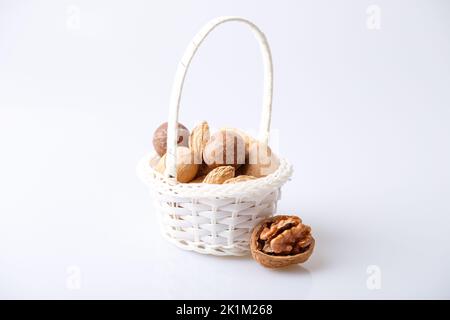 Assorted nuts in the shell on a white background: walnuts, pecans, almonds, macadamia. Nuts in a basket. Selective focus, close-up. Place for text. Stock Photo