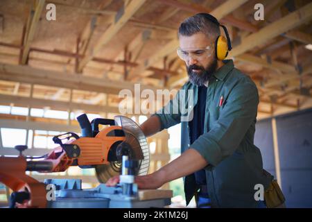 Construction worker working with eletric saw inside wooden construction of house, diy eco-friendly homes concept. Stock Photo