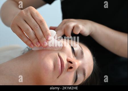 Cosmetologist does a facial massage with a gouache scraper. close up. Professional anti-aging facial massage.  Stock Photo