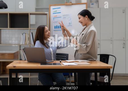 Happy business asian people are keeping arms raised hi five and expressing joyful while standing. achieving goals. Stock Photo