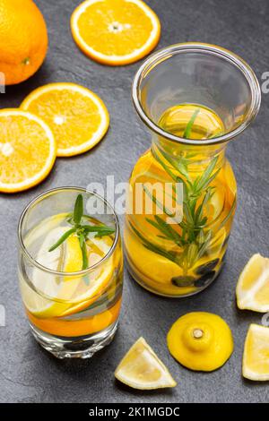 Infused summer drink with oranges, blueberries and rosemary in glass and bottle. Sliced orange slices on table. Top view. Black background Stock Photo