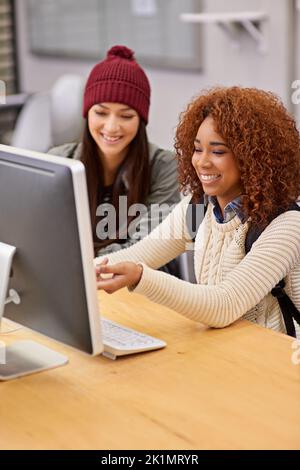 Using online resources to their advantage. two female students studying together at a computer in the library. Stock Photo