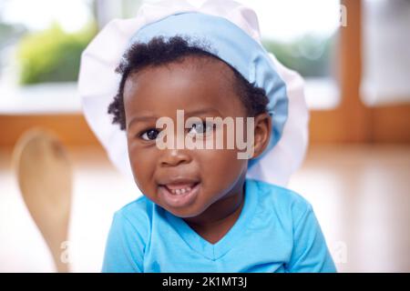 Can I cook something awesome for you. Portrait of an adorable baby boy wearing a chefs hat and holding a wooden spoon. Stock Photo