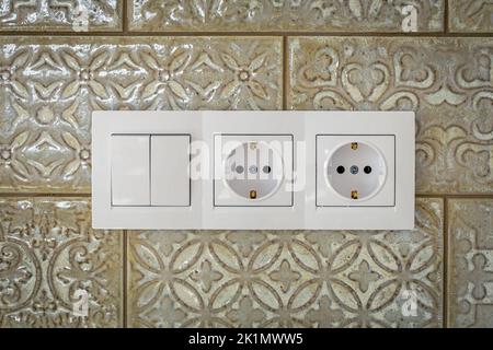 White plastic walk-through switches and sockets on a white wall. Stock Photo