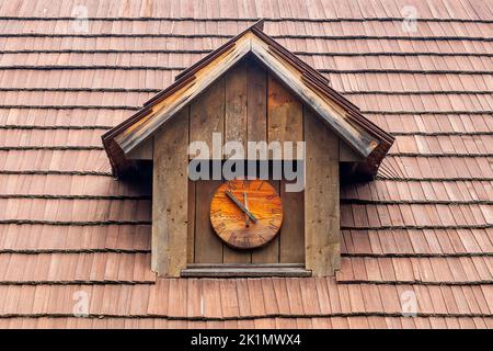 historic dormer with a wooden clock on a shingled roof Stock Photo