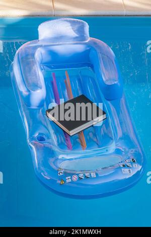 A black book rests on an inflatable pool mat floating on the water Stock Photo