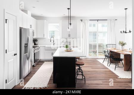 A modern farmhouse kitchen and dining rom with a black island, white cabinets, stainless steel appliances, and wooden table and chairs. Stock Photo