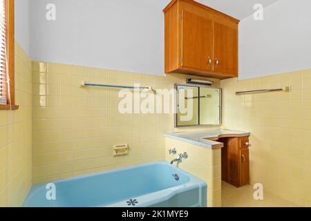 A dated bathroom with yellow tiled walls and floor and a blue bathtub. Stock Photo