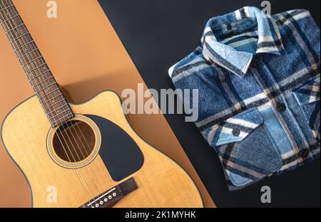 Acoustic guitar and plaid shirt on a colored background, flat lay. Stock Photo