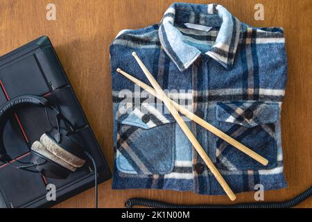 Headphones and folded plaid shirt and drumsticks on a wooden background. Stock Photo