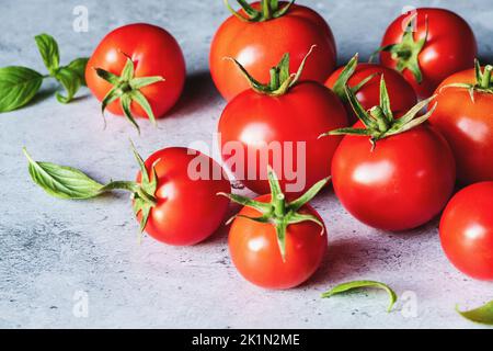 Red tomatoes with green basil leaves on gray concrete background, selective focus Stock Photo