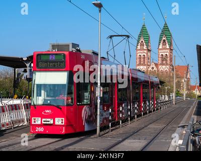 Freiburg im Breisgau, Germany - April 13, 2022: Red tram on the tram stop with a view of the Church of the Sacred Heart in the background Stock Photo