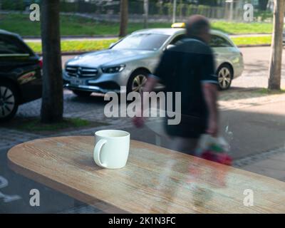 A man passes by a restaurant in Freiburg im Breisgau where there is an empty coffee cup on the table. Stock Photo