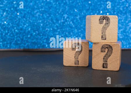 question marks on wooden cubes stacked on blue glitter background Stock Photo