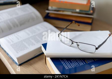 A pair of glasses and on a pile of printed books on a desk. Stock Photo