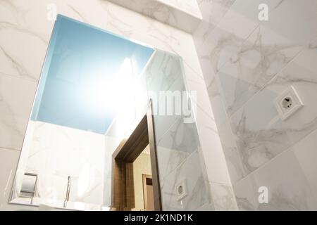 Reflection of the bathroom in the mirror and stretch blue ceiling, wall and ceiling in the bathroom, interior of the apartment Stock Photo