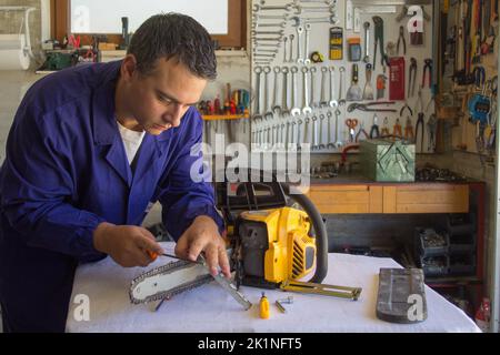 Image of a handyman who sharpens the chain of a chainsaw with a file. Preparation of tools for cutting wood in anticipation of winter. Do-it-yourself Stock Photo