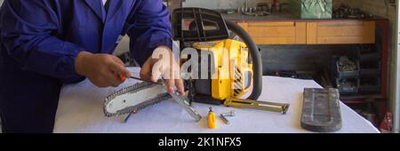Image of a handyman who sharpens the chain of a chainsaw with a file. Preparation of tools for cutting wood in anticipation of winter. Do-it-yourself Stock Photo