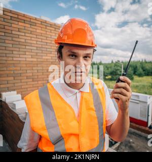 Foreman inspector or construction worker in hardhat portrait. Engineer in helmet with walkie-talkie in hand directs construction process. Stock Photo