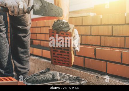 Worker at construction site applies cement mortar to brick for construction of brick house. Stock Photo