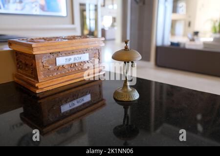 Brown wooden tip box with antique silver call bell on reception service desk counter, copy space. Stock Photo
