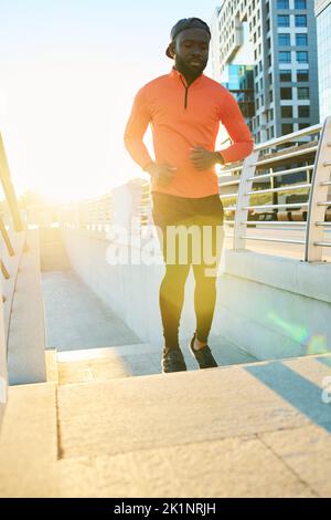 Young African American sportsman running along bridge in urban environment in the morning with sunlight behind Stock Photo