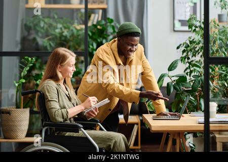 Young confident businessman pointing at laptop screen during presentation of project points to colleague making notes Stock Photo