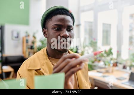 Young confident black man in casualwear pointing at transparent noticeboard while making presentation of his ideas Stock Photo