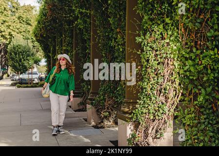 Young woman walking on the street holding a mesh bag with vegetables on her shoulder. Sustainable shopping, modern lifestyle Stock Photo