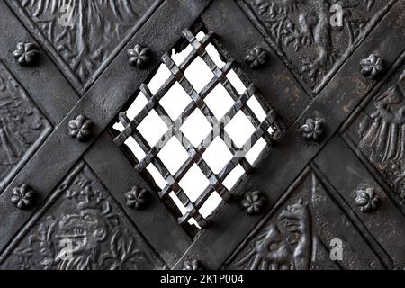 A medieval metal door with small window with grid, wrought and grooved, close up. Stock Photo