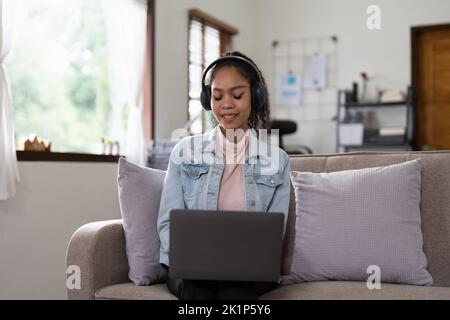 Young woman sitting on sofa at home video call chatting with friends using a laptop at home. Stock Photo