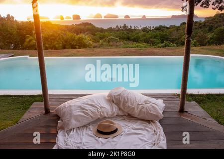 Traveler hat on white bed against Beautiful ocean view background, Tourists relaxing in tropical resort with swimming pool. travel summer, vacation an Stock Photo