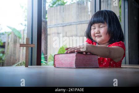 Little girl praying on bible at home, child's pure faith Stock Photo