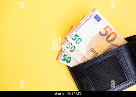 Fifty euro banknotes inside a black wallet on yellow background Stock Photo