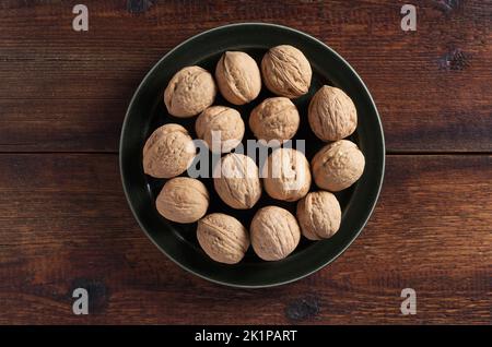 Whole walnuts in dark plate on a wooden background, top view Stock Photo