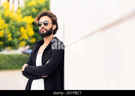 young man with sunglasses leaning in a white wall Stock Photo