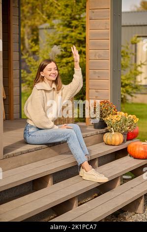 Joyous lady seated on the veranda stairs greeting someone Stock Photo