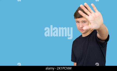 Stop gesture. Refusal sign. Offer rejection. No thanks. Portrait of annoyed teen guy in black t-shirt showing hand open palm looking at camera isolate Stock Photo