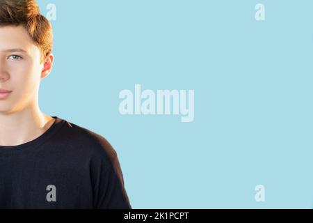 Teen lifestyle. Commercial background. Independence success. Half face portrait of shy calm guy in black t-shirt looking at camera isolated on blue em Stock Photo