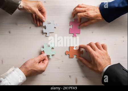 Four business people holding matching puzzle pieces of various pastel colours in a conceptual image of business teamwork and cooperation. Stock Photo