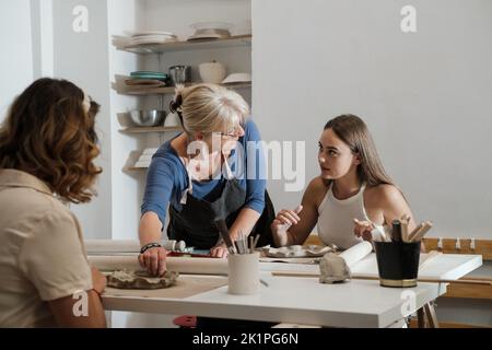 Learning on Pottery workshop in studio. People working with clay on the table. Adults working with ceramic plates. Pottery as hobby and leisure Stock Photo